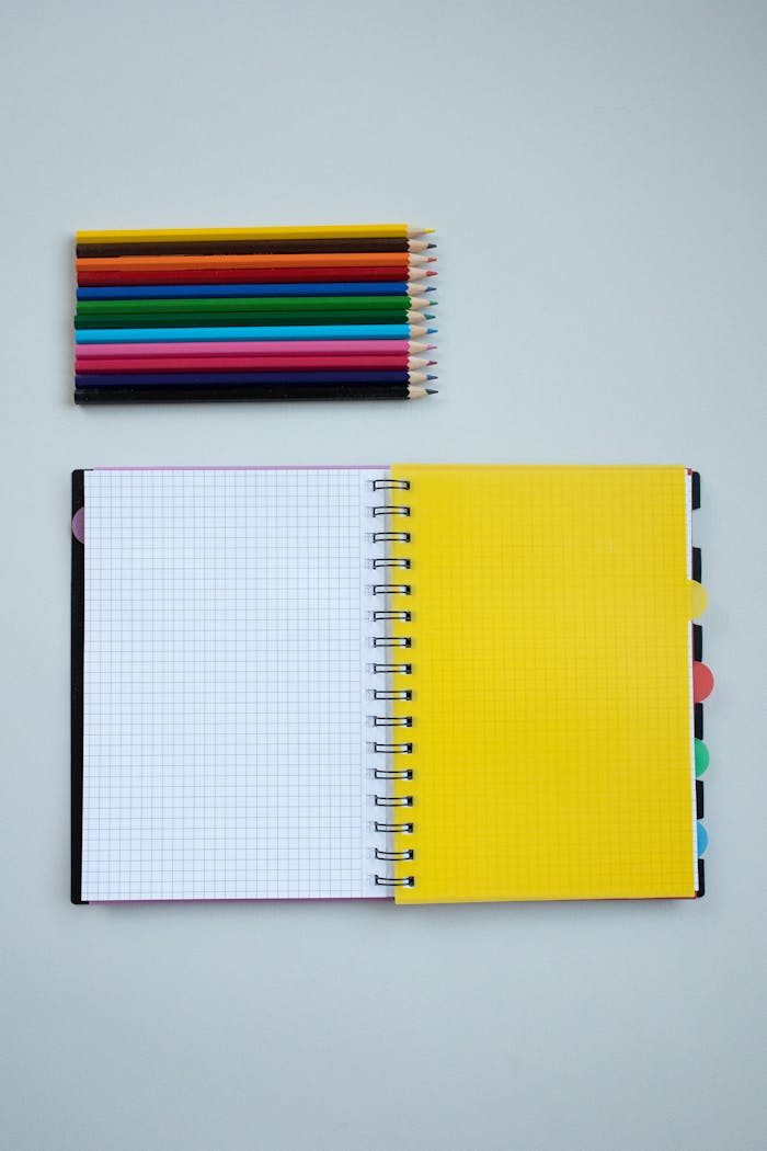 Colorful pencils and a spiral notebook on a white surface, ideal for back-to-school themes.
