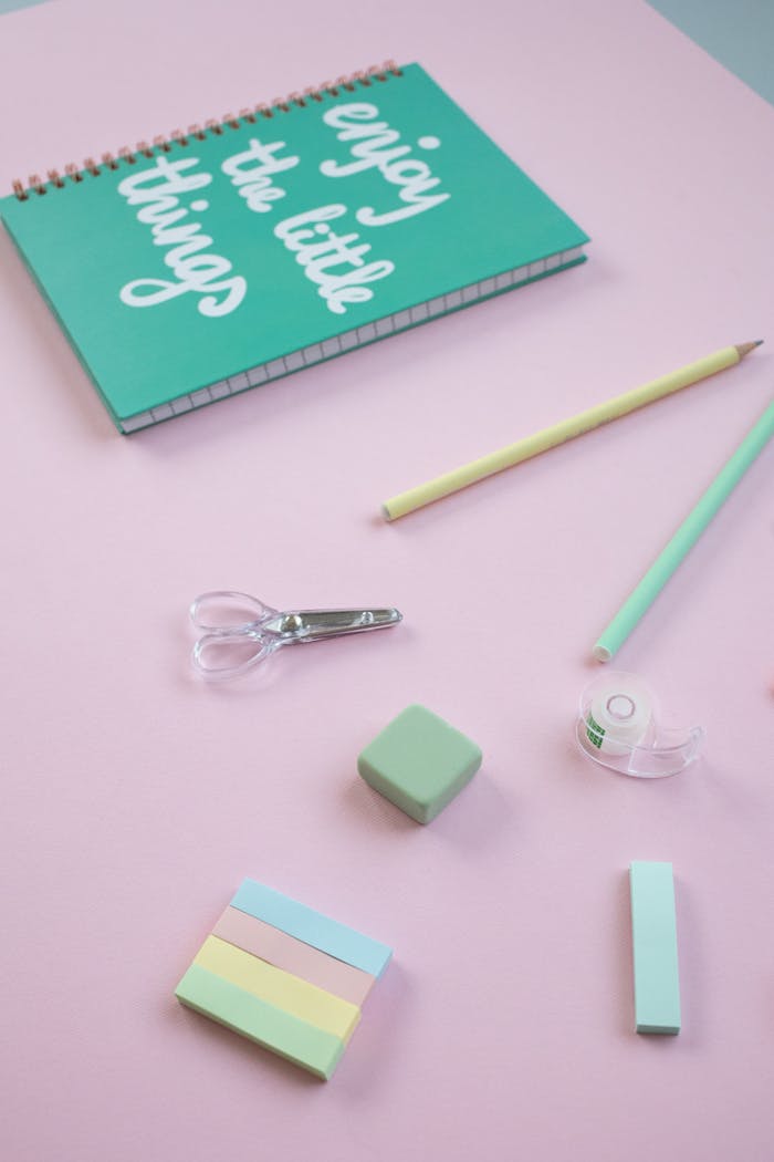 services-01 A flat lay of pastel school supplies on a pink surface featuring a notebook and stationery.