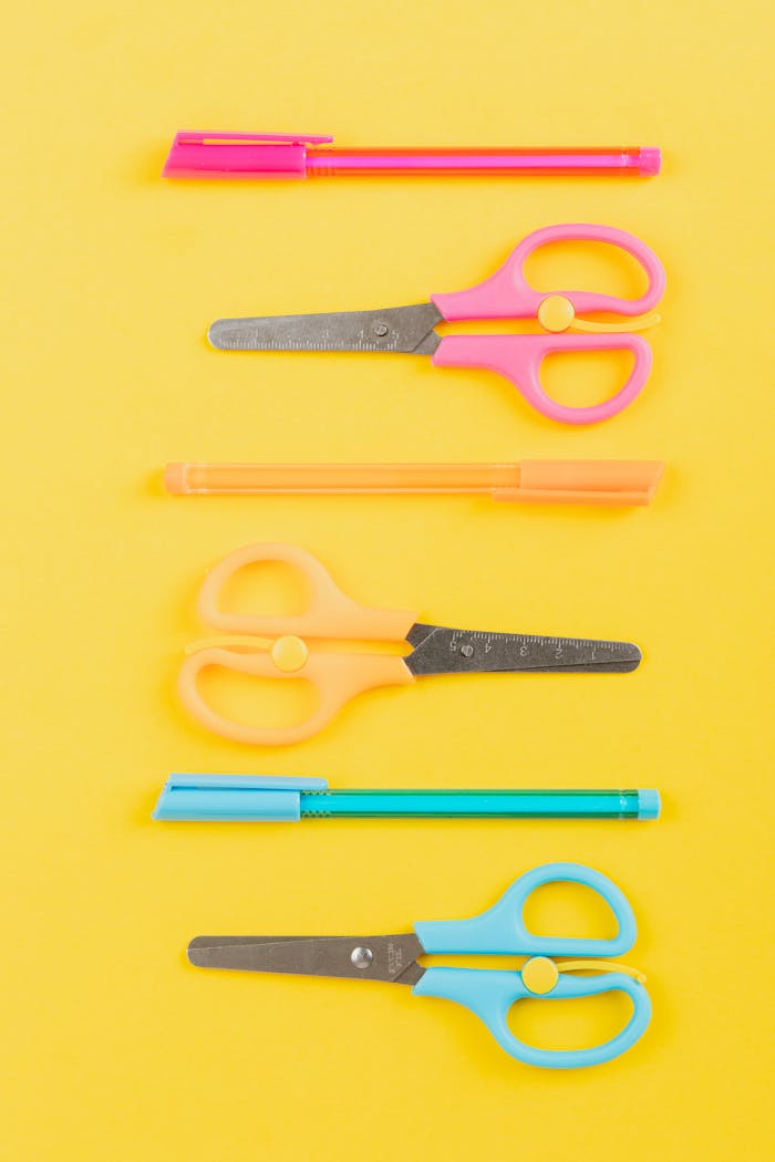 about-img Vibrant flat lay of pens and scissors on a yellow backdrop enhancing study aesthetics.